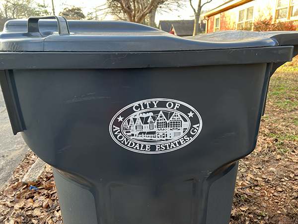 grey trash bin with the City of Avondale Estates logo in white with house in the background