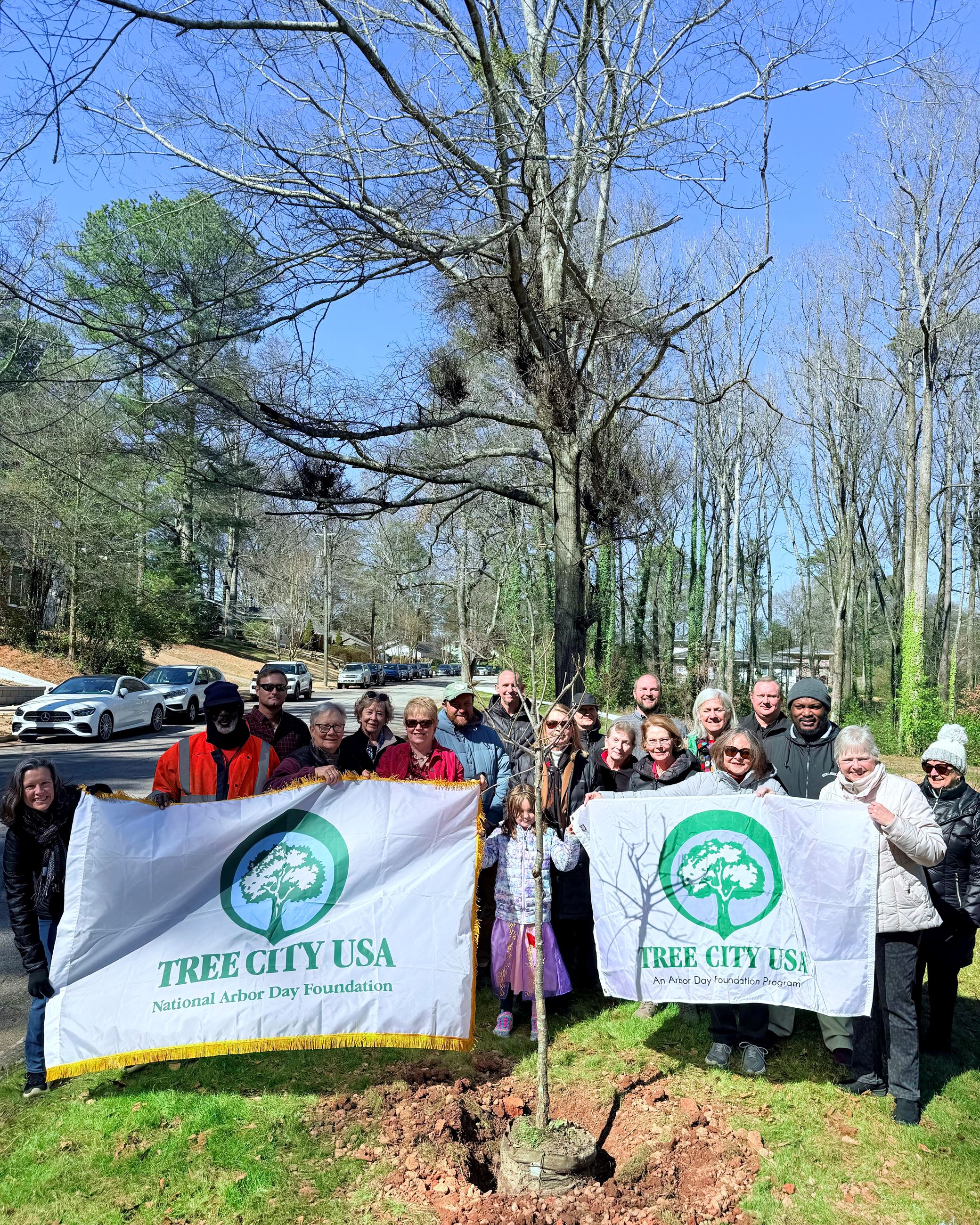 2025 Tree City USA planting with city staff, residents, and members of the AEGC holding banners