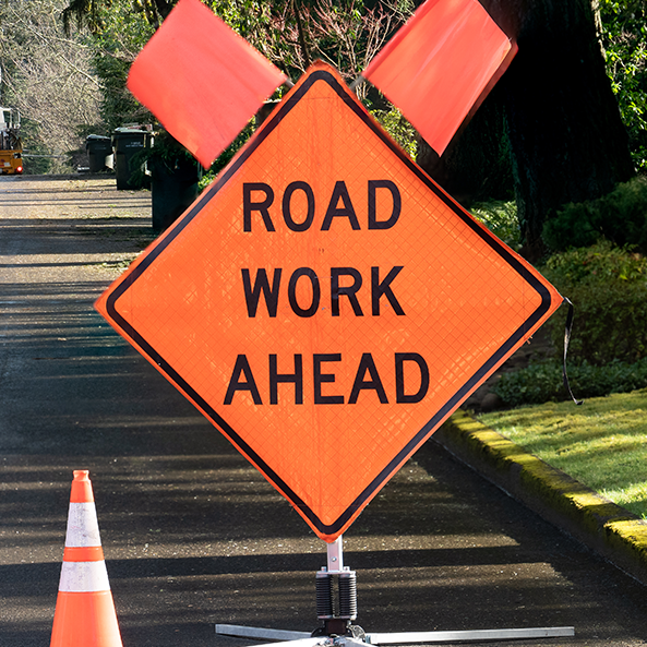 Orange Roadwork Ahead street sign with flag and cone in the road